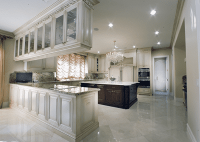 An upscale kitchen with marble flooring, white cabinetry, and granite countertops featuring a central island and modern appliances.